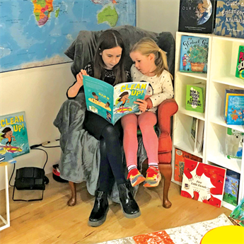 Two girls reading a book called 'Clean up' together, surrounded by more colourful books about environmental action