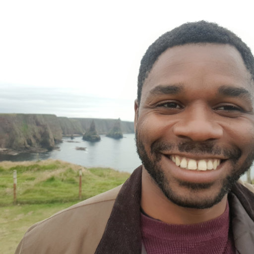 Headshot of a black man in a coat smiling in a field