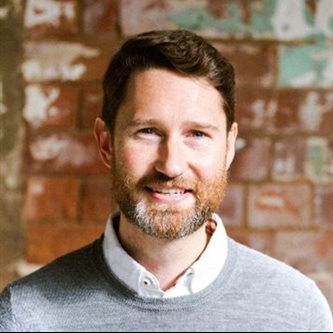 headshot of a white man smiling in front of a walll