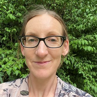White woman in glasses smiling in front of a tree