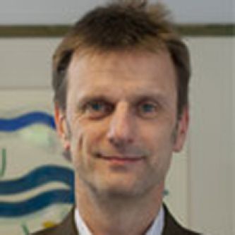 headshot of a white man with brown hair in a suit smiling