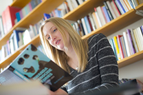 Female student reads a book in an office, in front of a bookcase