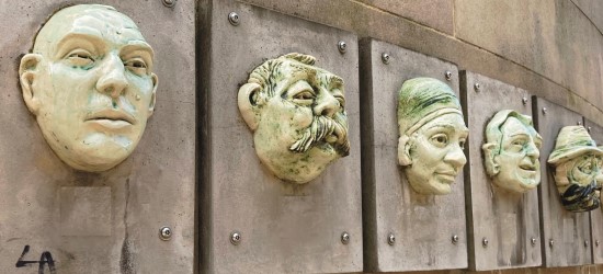 5 sculptures of faces lined up in a row on a wall