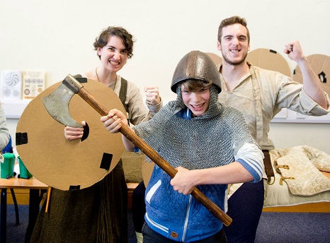 Photo with young bog wearing a helmet and holding an axe in the foreground while two older volunteers stand behind