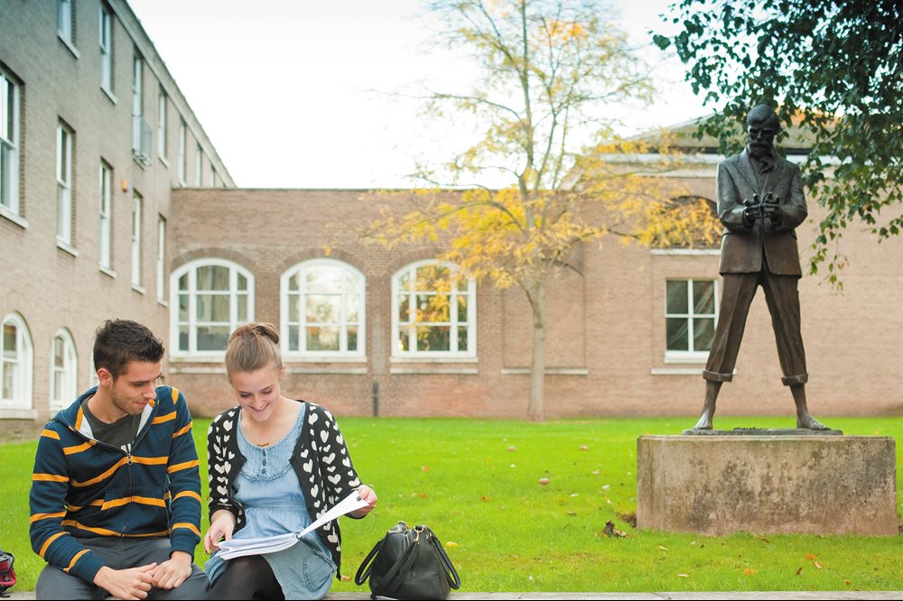 Two students sat on the wall outside the LASS building on University Park campus in front of the DH Lawrence statue