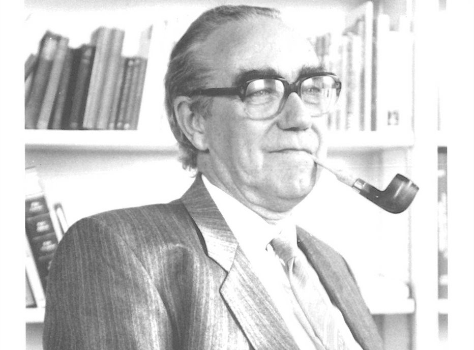 Black and white photograph of an older white man wearing glasses, a suit and smoking a pipe.