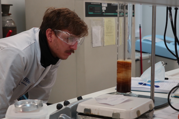 Scientist in goggles inspecting boiling glass cylinder of coffee
