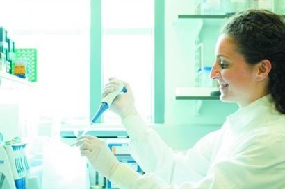 Smiling woman in lab-wear using a pipette