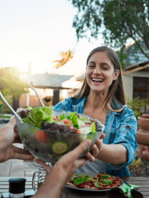 Social, woman and salad in backyard for lunch, sharing and healthy meal in summer. Female person, food and friendship on estate for birthday party, reunion and happiness at outdoor table at house