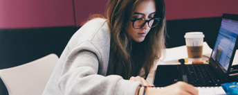 Student making notes whilst looking at a laptop