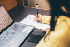 close up of a student writing in a notebook in front of her laptop