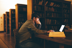 male student looking pensively at a laptop in an dark library