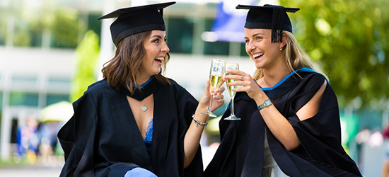 Two female students enjoying a drink in their graduation gowns
