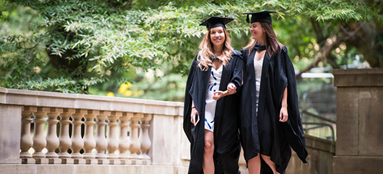 Two female students on bridge celebrating graduation in their gowns