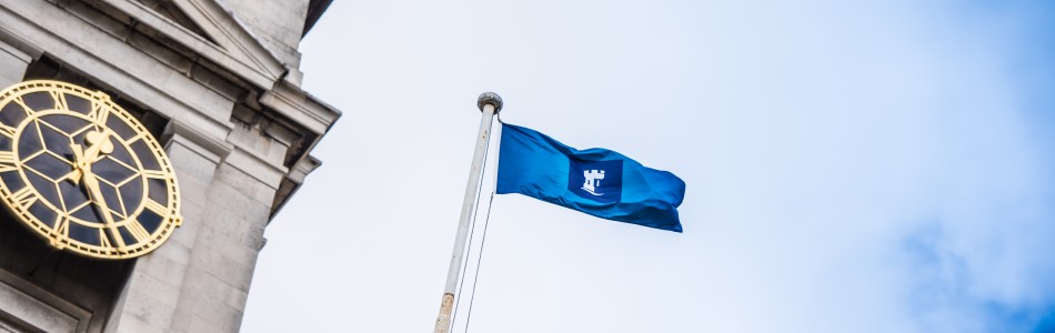 Blue flag with University logo, flying next to a clock tower