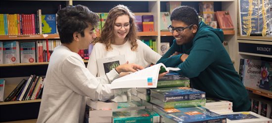 Three students chatting around pile of books in bookshop