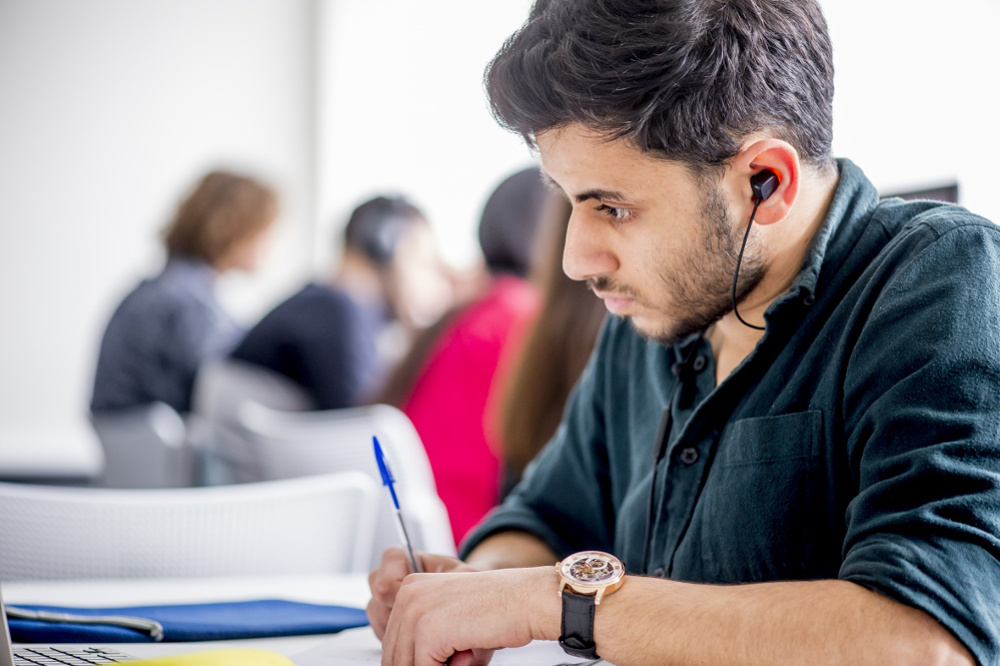Student wearing earphones and writing notes