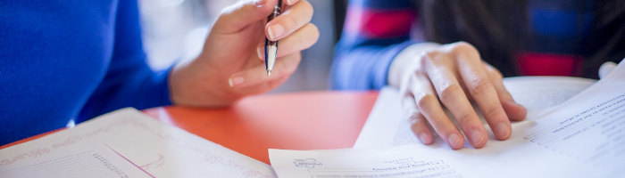 Close-up photograph of two people's hands reading and writing on paper