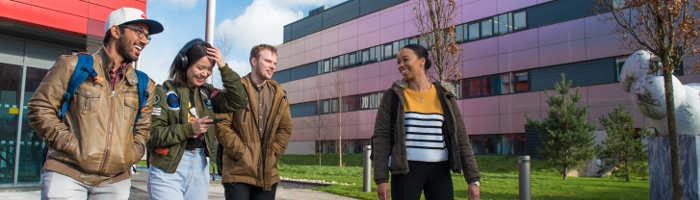 Photograph of four students walking and smiling outside on campus