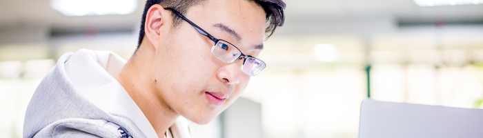 Close-up photograph of a bespectacled student using a laptop