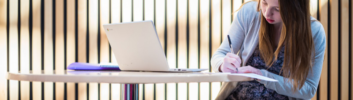 Photograph of a student writing notes while using their laptop