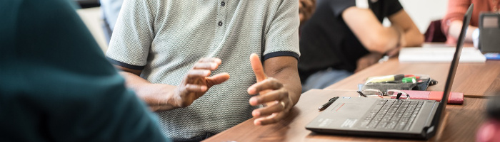 Close-up photograph of a student using hand gestures to explain, while working from a laptop