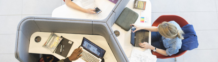Photograph of three students using a study space (taking notes and working on laptops), as viewed from above